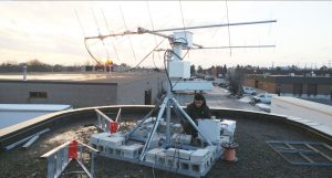 A technician works with satellite technology and other equipment on a rooftop. Cheaper Telecom Service from Cellphone Towers in Space