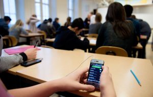 student hands hold cellphone at school desk