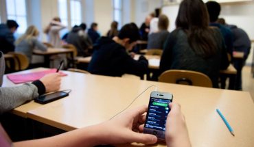 student hands hold cellphone at school desk