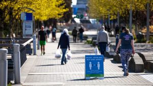 people walking outdoors, sign shows slocial distancing reminder notice