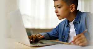 young male student looks at his laptop screen, pencil in hand