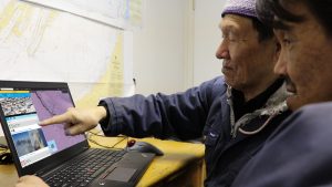 two Inuit men look at computer screen in office