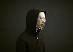 man in hoodie, looking off to right, wears transparent plastic face mask