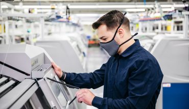man wearing mask looks at industrial machine