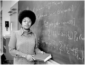 young black woman in glasses stands at blackboard