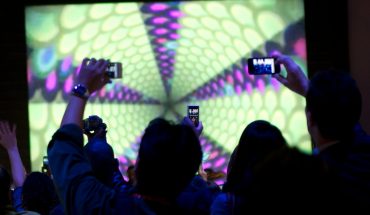 people hold up smartphones near illuminated display