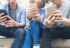 young people sit together as they look at their smartphones