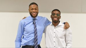 two young Black men with arms around each other smile at camera