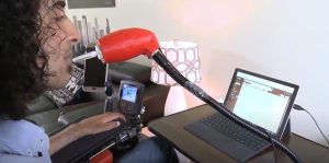 man sits at computer screen, blowing into LipSync assistive technology device. 