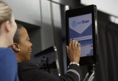 Two women use airplane boarding program shown on tablet screen.