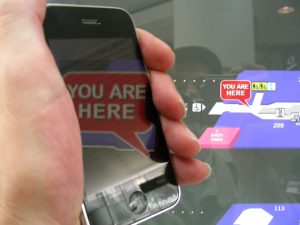 hand holds smartphone, screen show words You Are Here