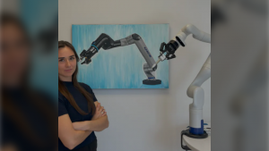 woman stands next to robotic arm with framed picture of robot wall