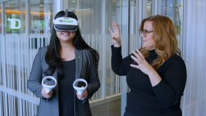 woman wearing VR headset, holding hand controllers, interacts with tech trainer
