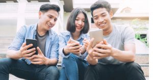 three young people sit smiling looking at smartphones