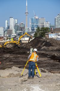 man with surveying tools on construction site; CN Tower in background