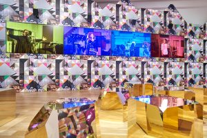 four giant video screens in art exhibit, photo murals and shiny floor stools visible