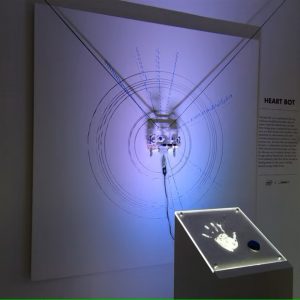 sensor podium with hand print in front of robotic arm and artwork on wall