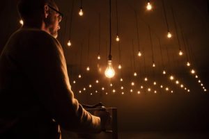 man at left in darkened room full of light bulbs