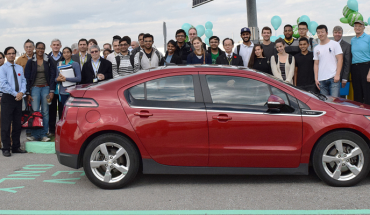 college students standing around a parked electric vehicle