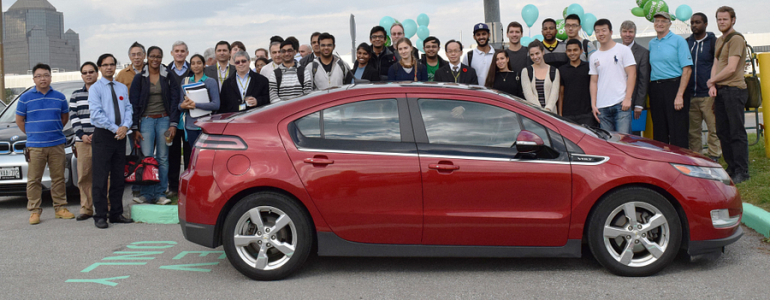 college students standing around a parked electric vehicle