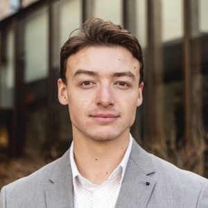 man in open shirt and jacket looks at camera