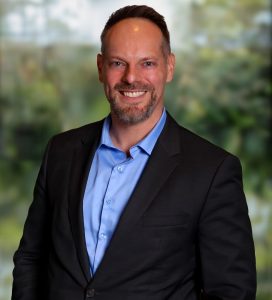 man in open shirt and jacket smiles to camera