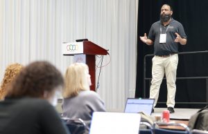 man on stage makes presentation to audience