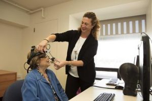 woman standing adjusts eye tracking technology on the head of seated woman