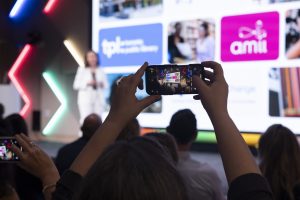 hands hold up smartphone taking picture of woman speaker on stage