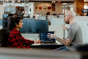 office workers seated in discussion, computers and desks in background