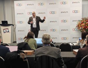 man on stage speaks to business crowd